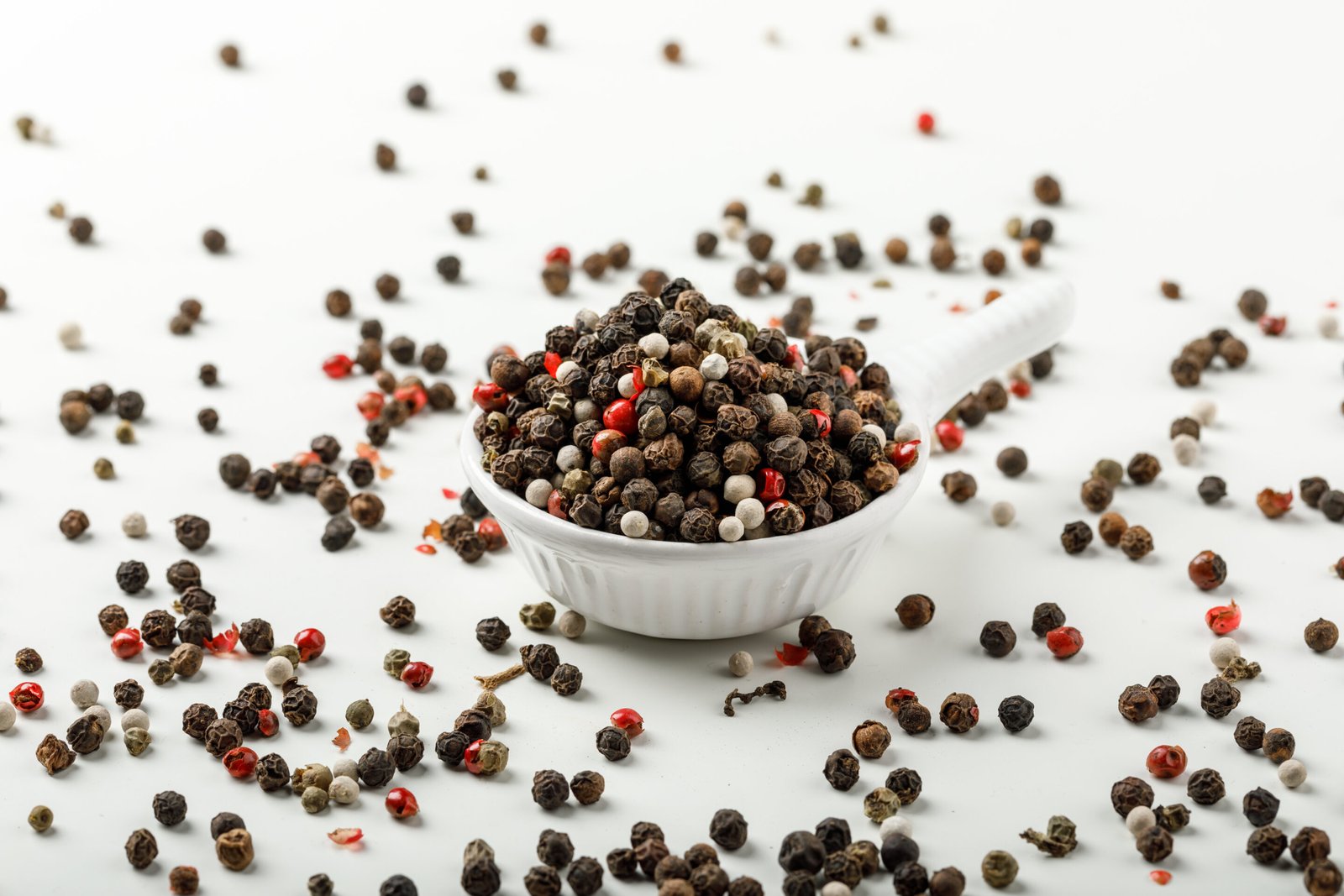 Mixed peppercorns in a white scoop side view on spicy and white background
